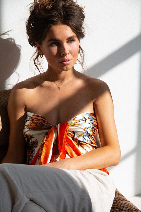 Foto van sjaal ANNA, een met fris oranje kleur geaccentueerde sjaal met elegant ketting-ontwerp gedragen als topje.